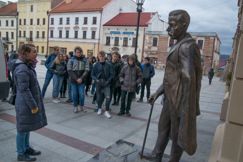 Grupa uczniów podczas zwiedzania Tarnowa. Stoją przy rzeźbie burmistrza Tadeusza Tertila